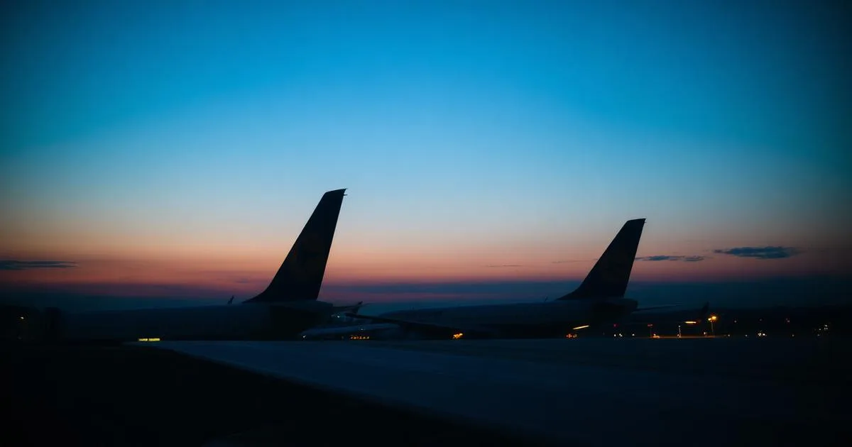 Two aircraft tails visible above an airport terminal roof at dusk